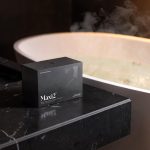 A premium packed box of Maxi2 longevity supplement sitting on a marble counter next to a warm evening downregulation bath
